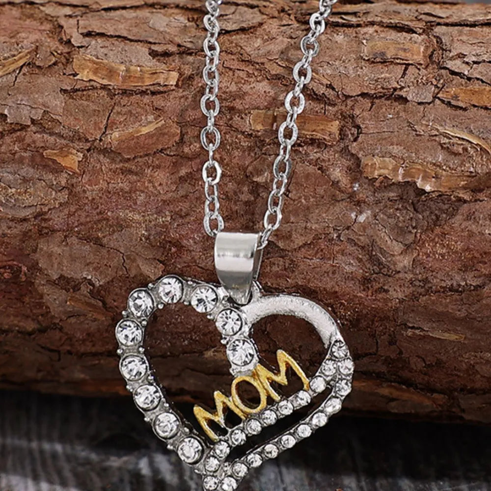 Heart-shaped pendant with 'MOM' on a silver chain against a wooden background