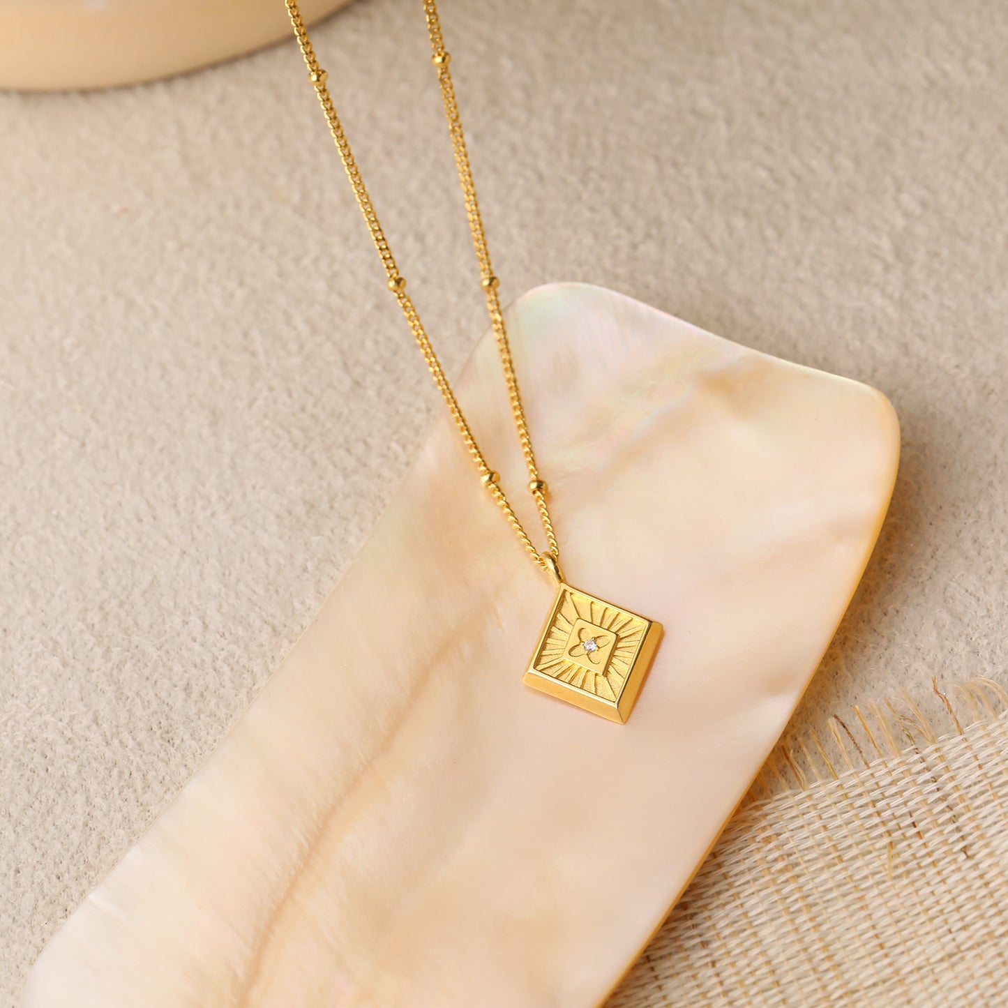 Gold necklace with a square pendant on a beige stone surface