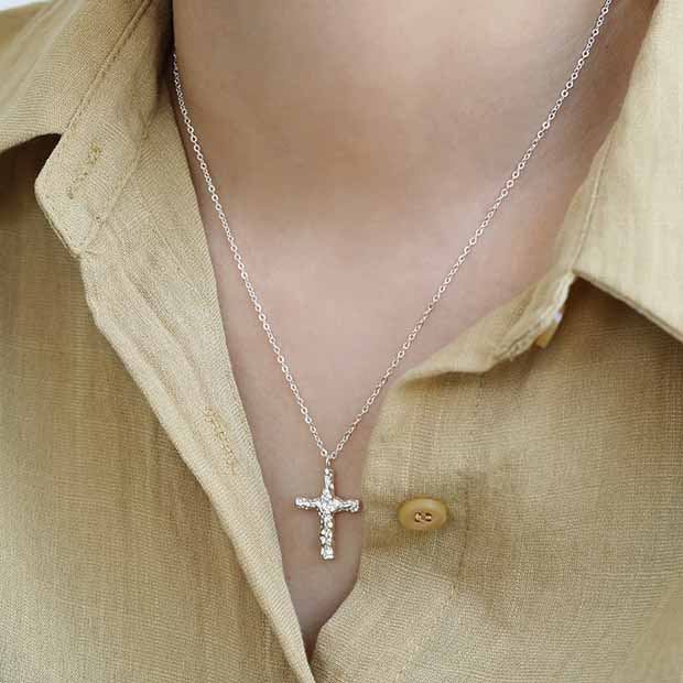 Silver cross necklace worn by a person in a beige shirt.