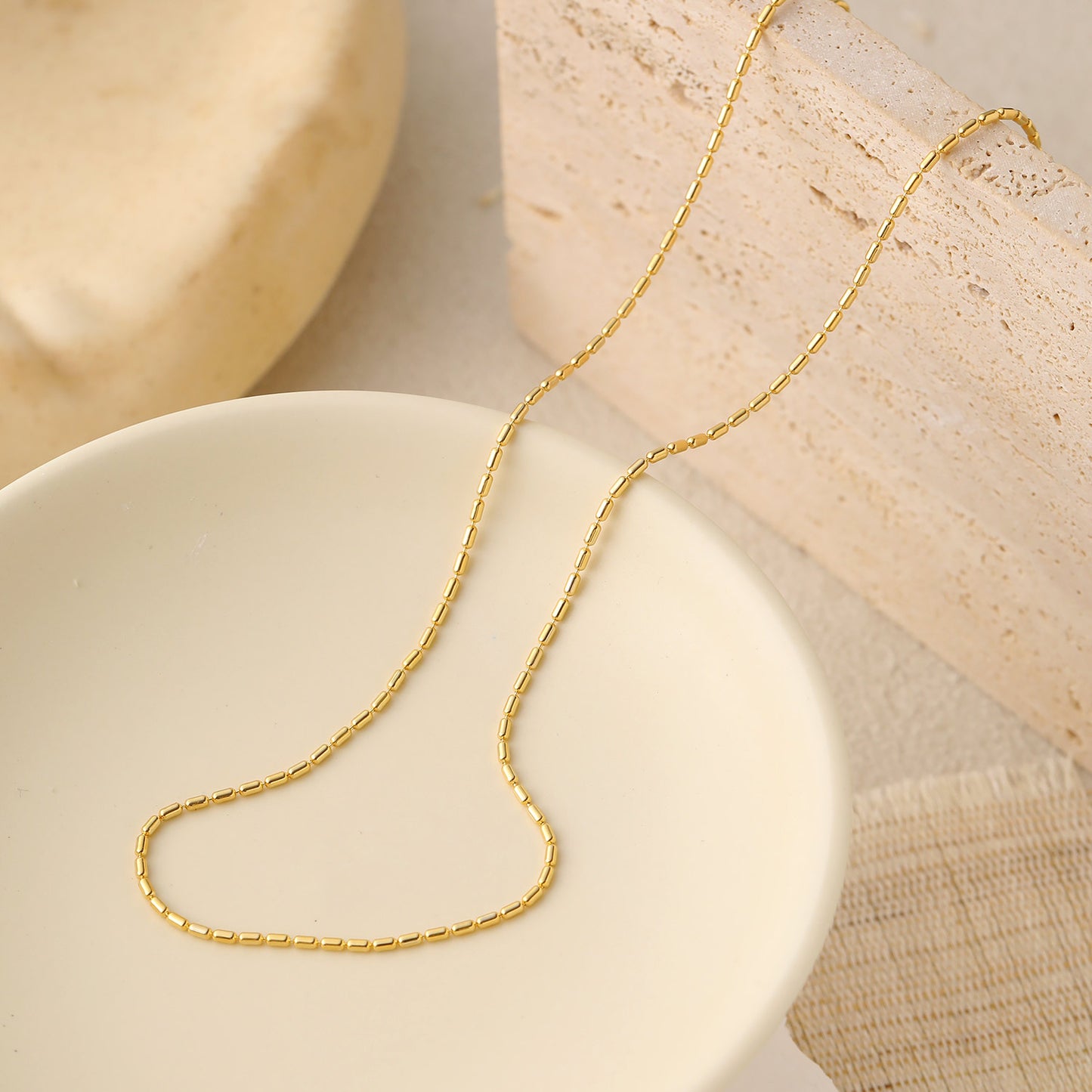 Gold chain necklace on a white dish with beige background