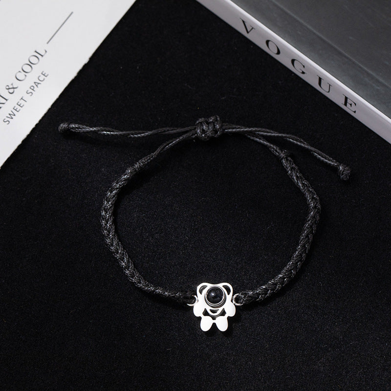 Black braided bracelet with a silver charm on a black surface with 'Vogue' magazine.