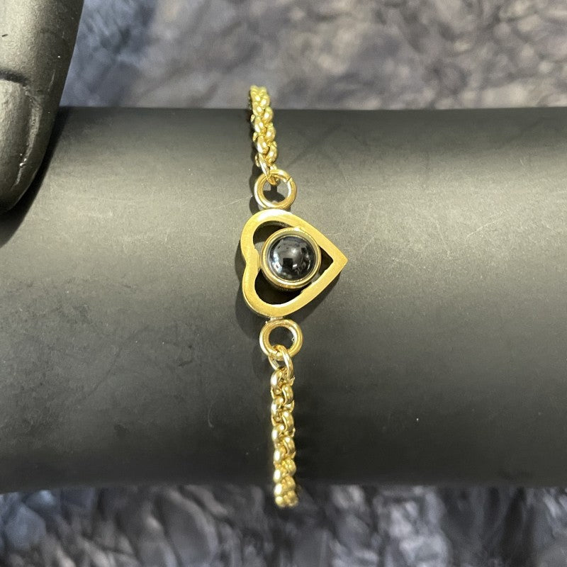 Gold bracelet with a heart-shaped clasp and black gemstone on a dark surface