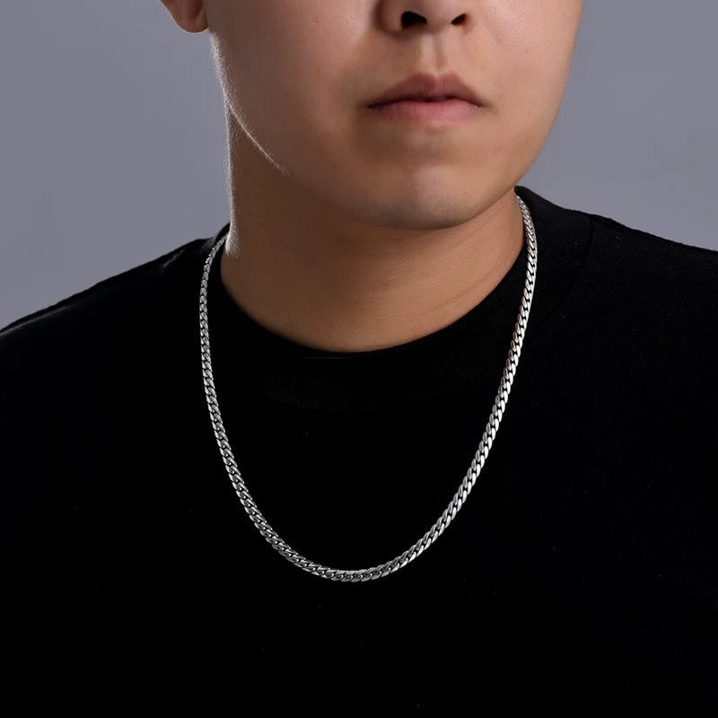 Person wearing a silver chain necklace against a gray background