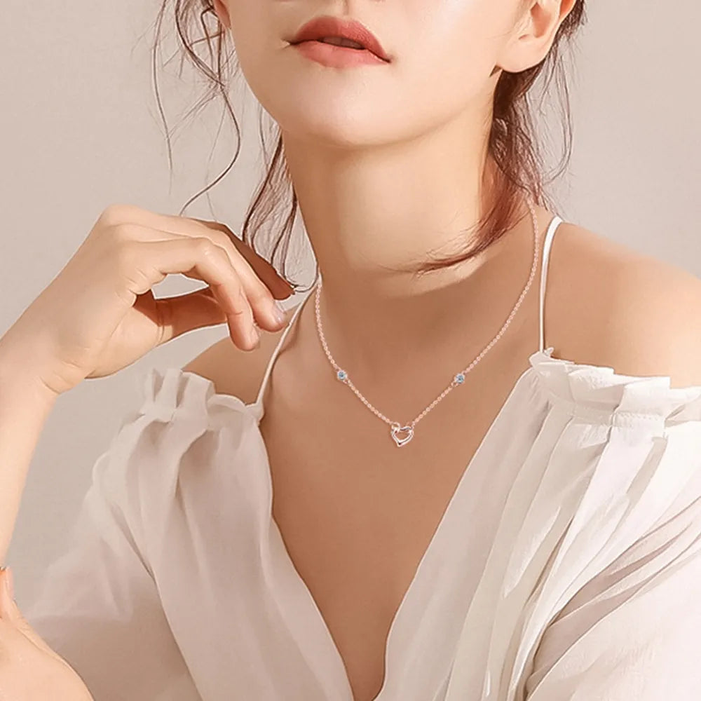 Woman wearing a delicate necklace with a heart design against a neutral background