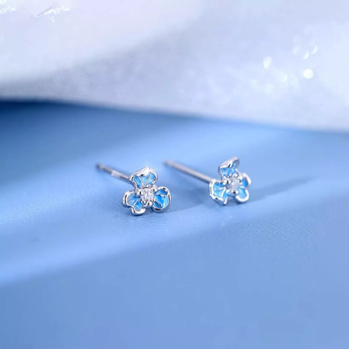 Flower-shaped earrings with blue gemstones on a light blue background