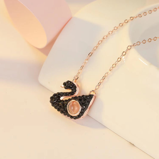 Rose gold swan-shaped necklace with black gemstones on a soft pink background