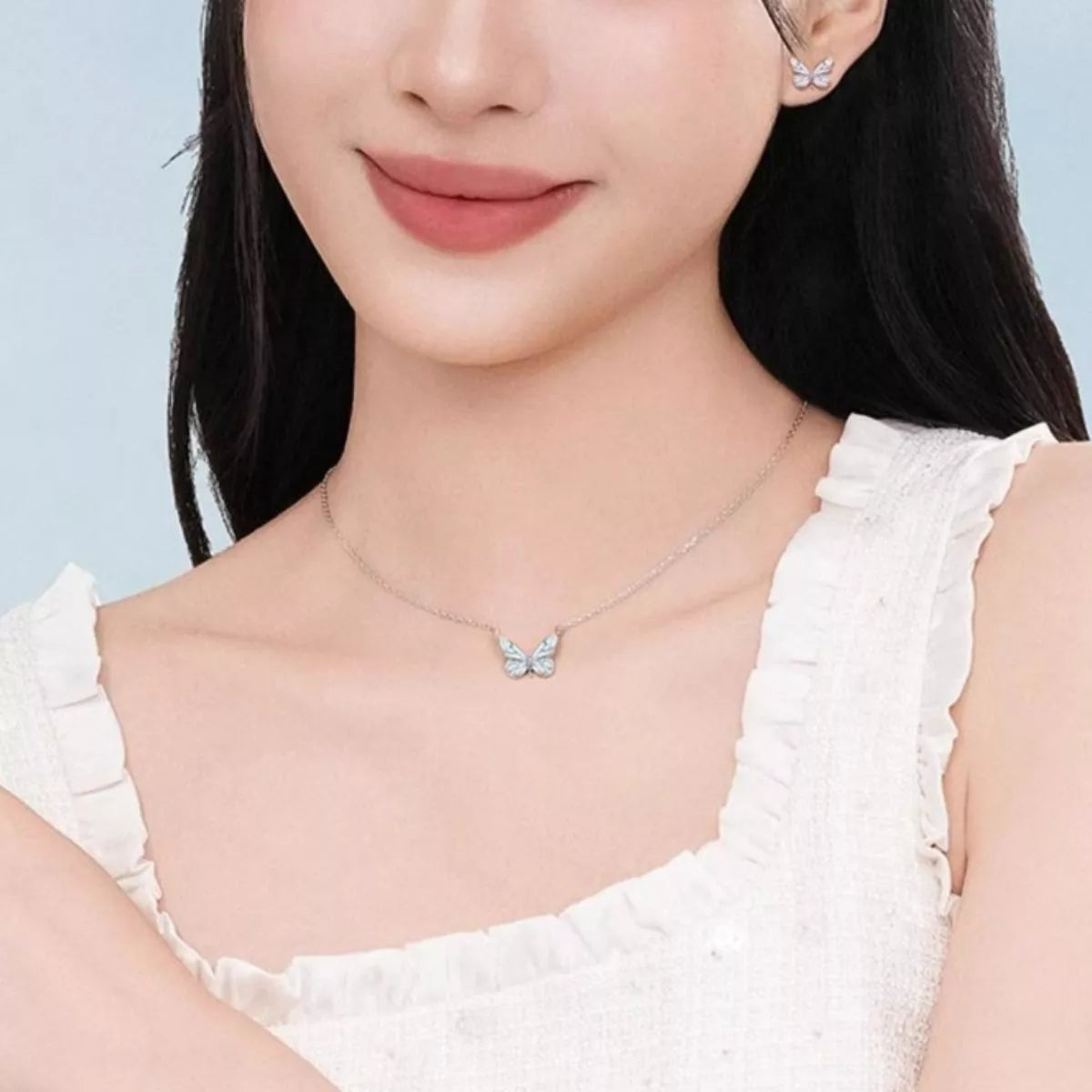 Woman wearing a butterfly necklace and earrings against a light blue background