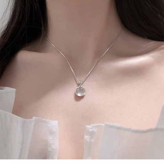 Silver necklace with a round pendant on a model wearing a white blouse.