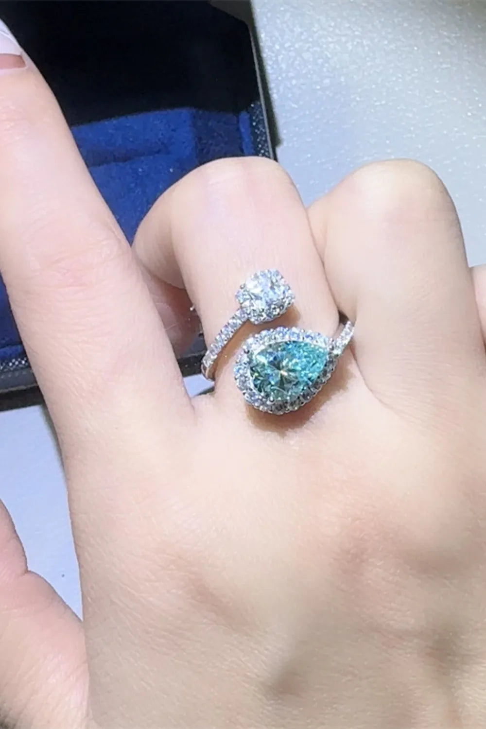 Close-up of a hand wearing a ring with a blue gemstone on a light background