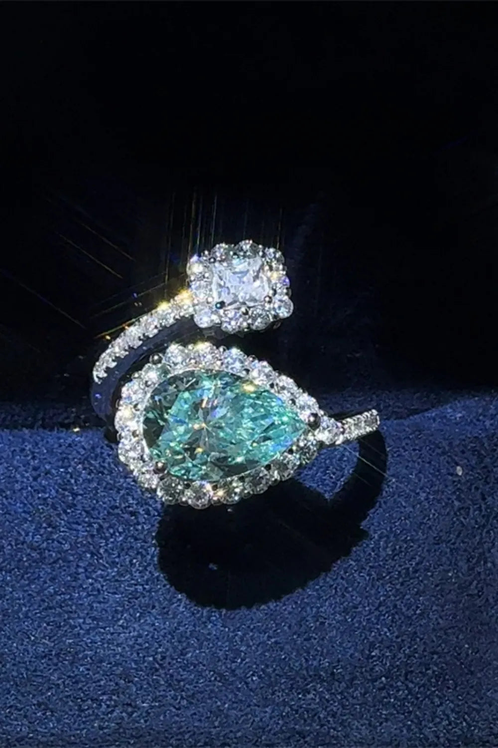 Two diamond rings, one with a pear-shaped green gemstone and the other with a square-cut gemstone, on a dark background.