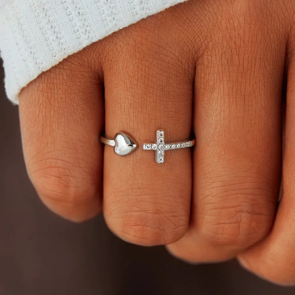 Close-up of a hand wearing two rings with heart and cross designs.