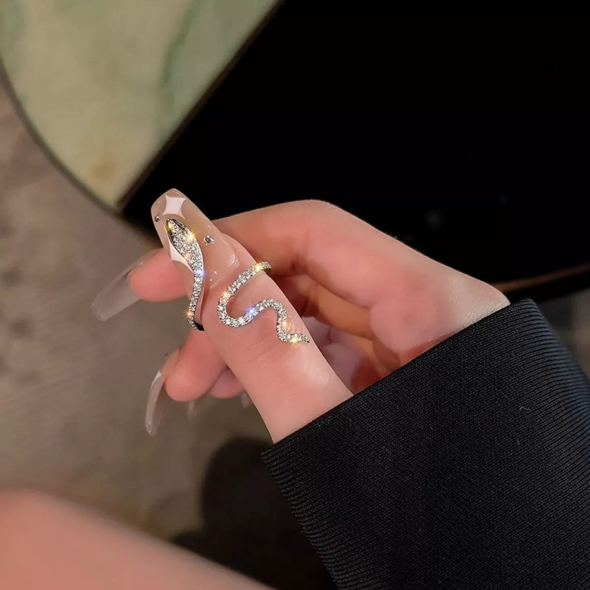 Hand holding a clear nail art with gold decorative elements against a blurred background
