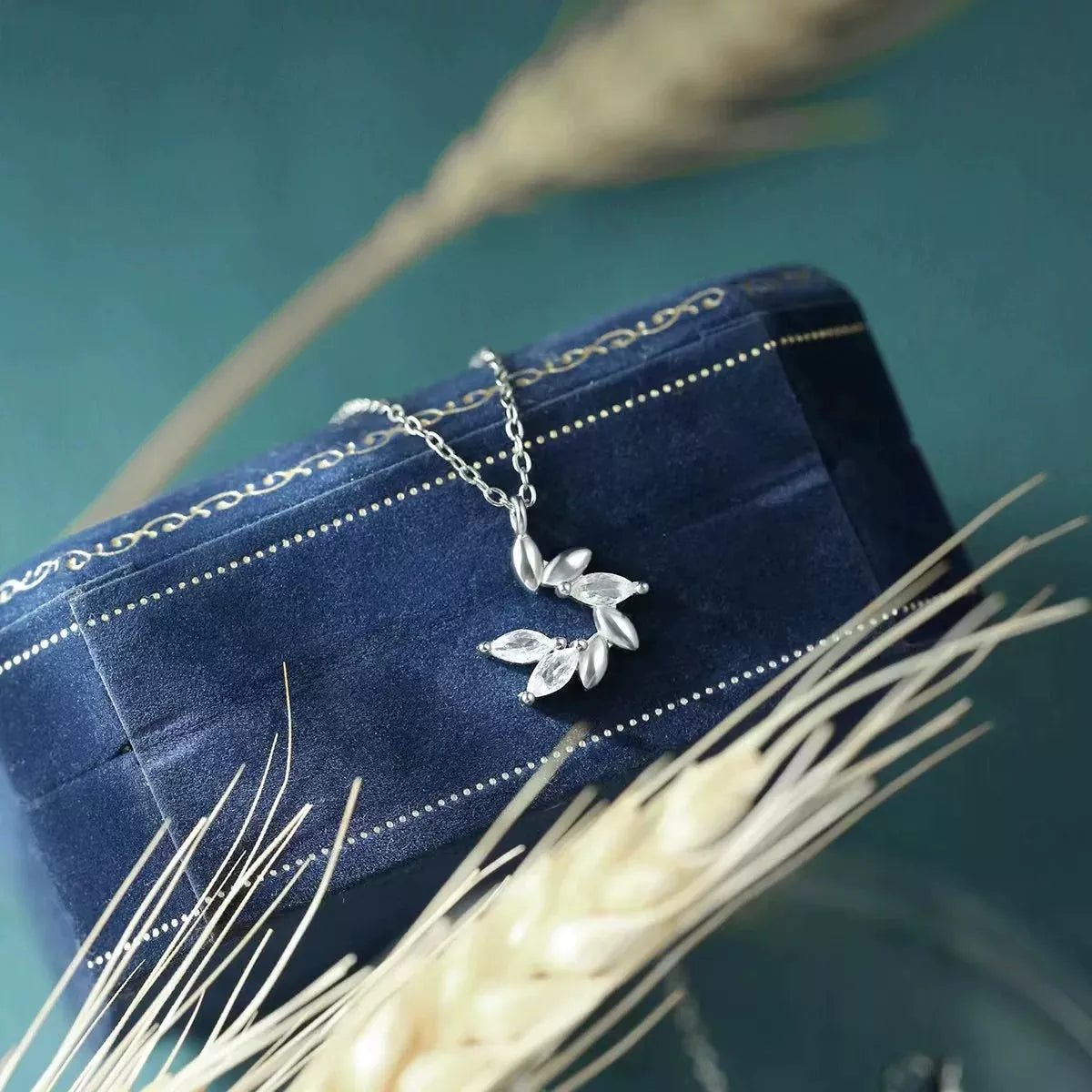 Silver leaf necklace on a blue velvet box with dried plants around