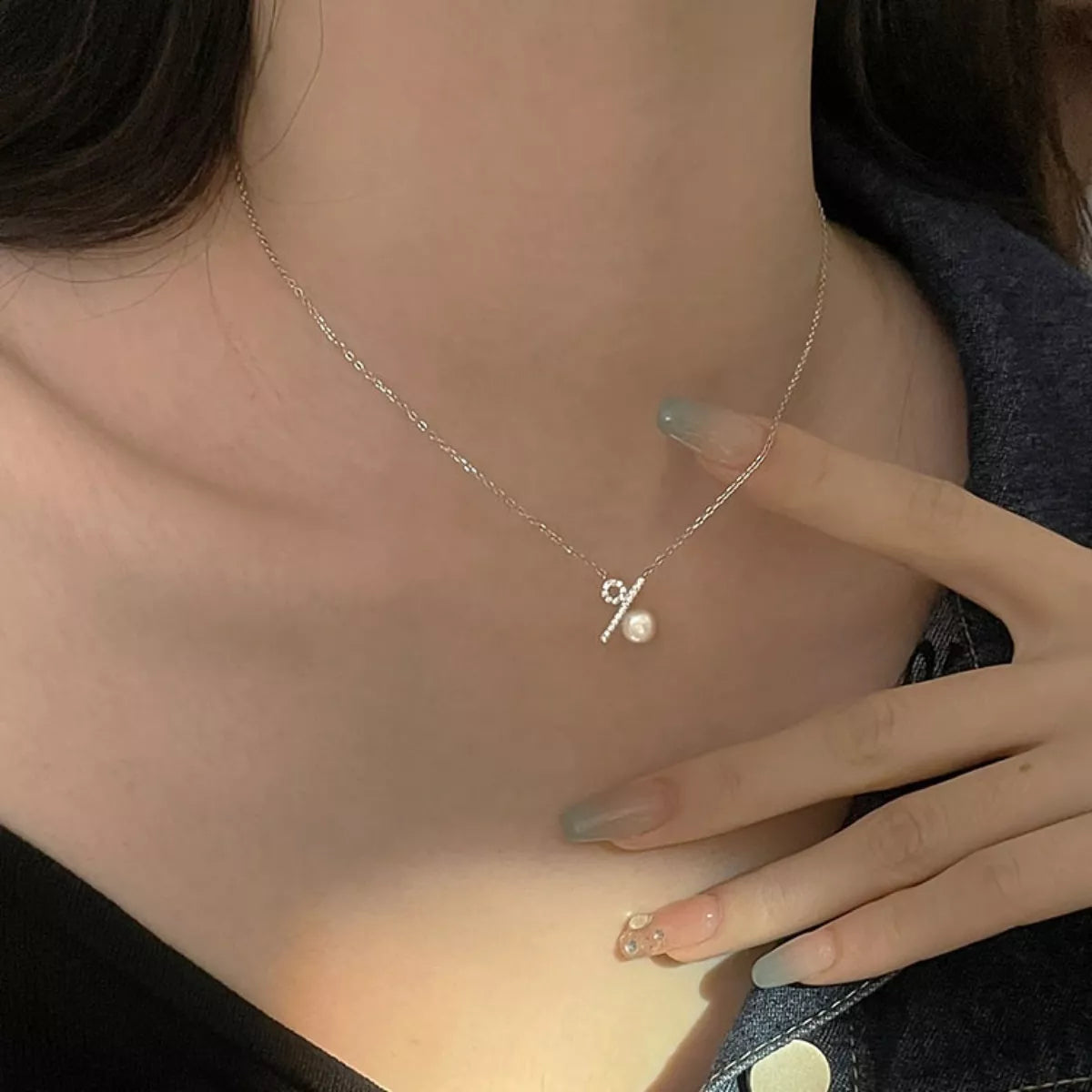 Necklace with a small pendant worn by a person, with a hand touching the neck.