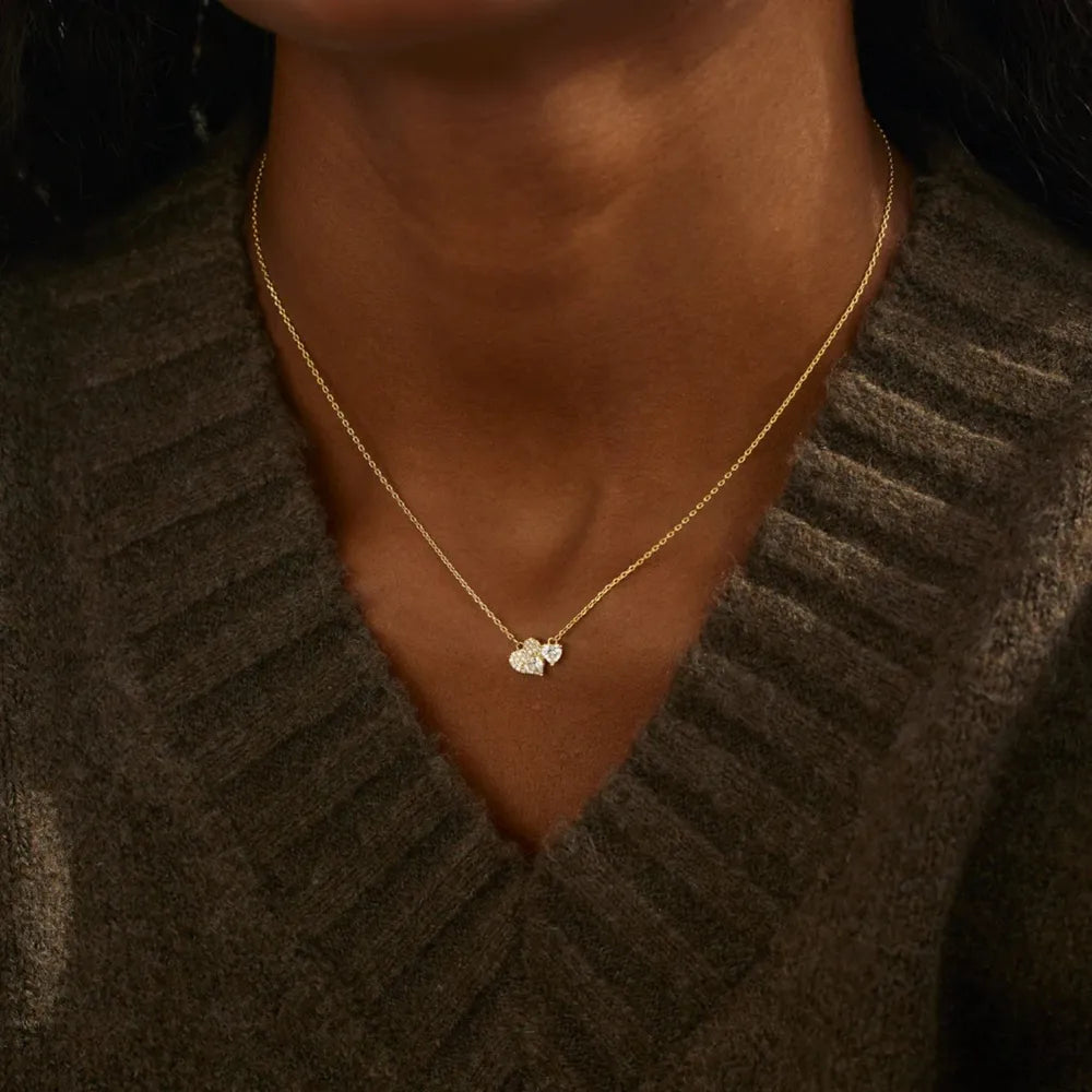 Gold necklace with a heart pendant worn by a person in a brown sweater.