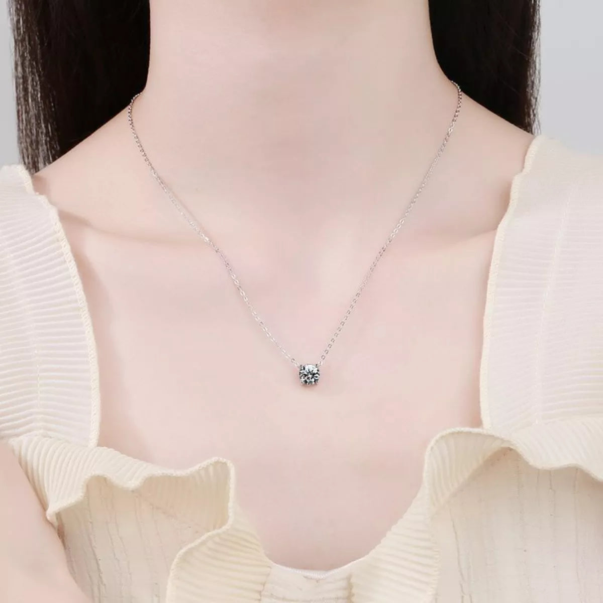 Silver necklace with a pendant worn by a person in a light-colored top.