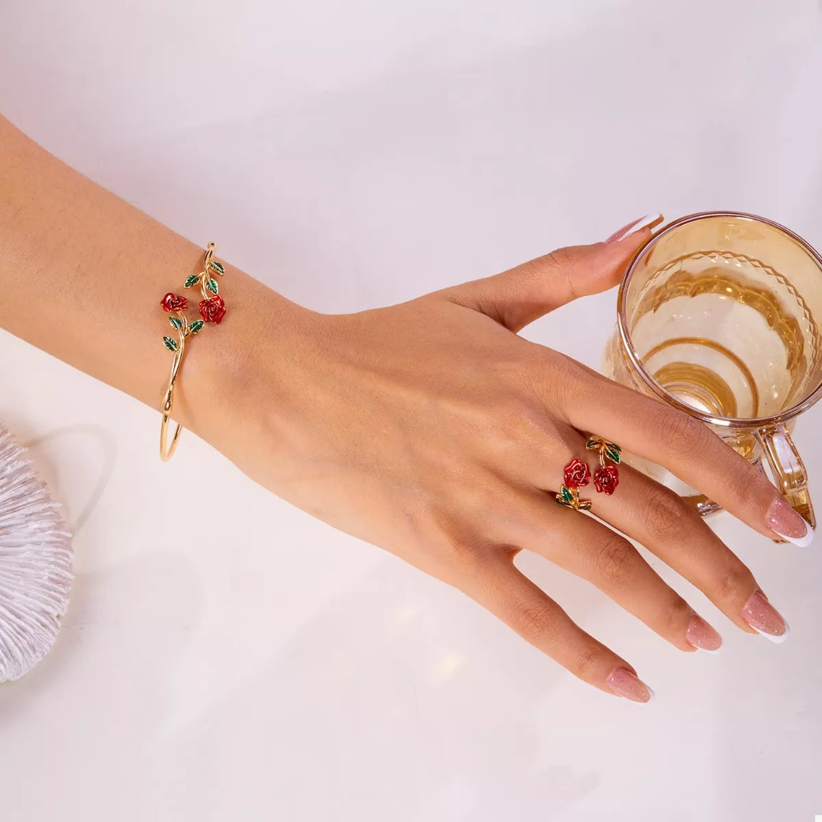 Hand wearing a bracelet and ring with a glass of coffee on a white background