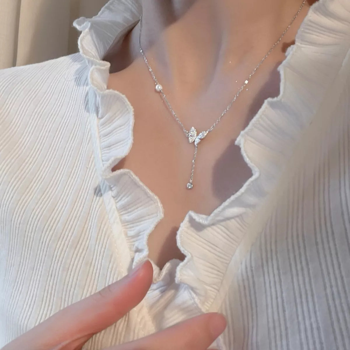 Silver necklace with a butterfly pendant worn by a person in a white blouse.