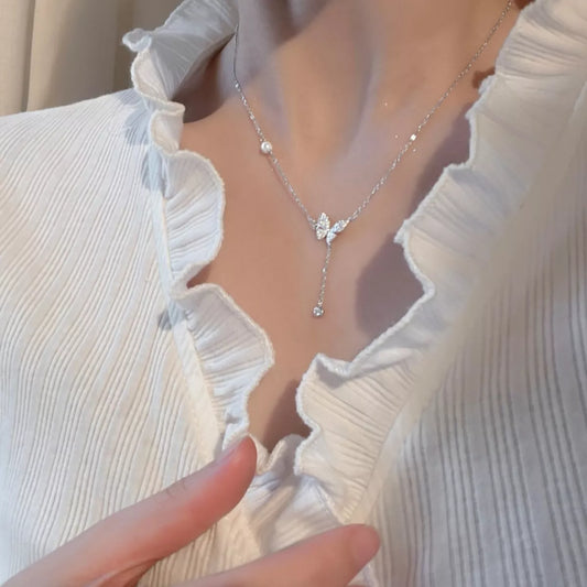 Silver necklace with a butterfly pendant worn by a person in a white blouse.