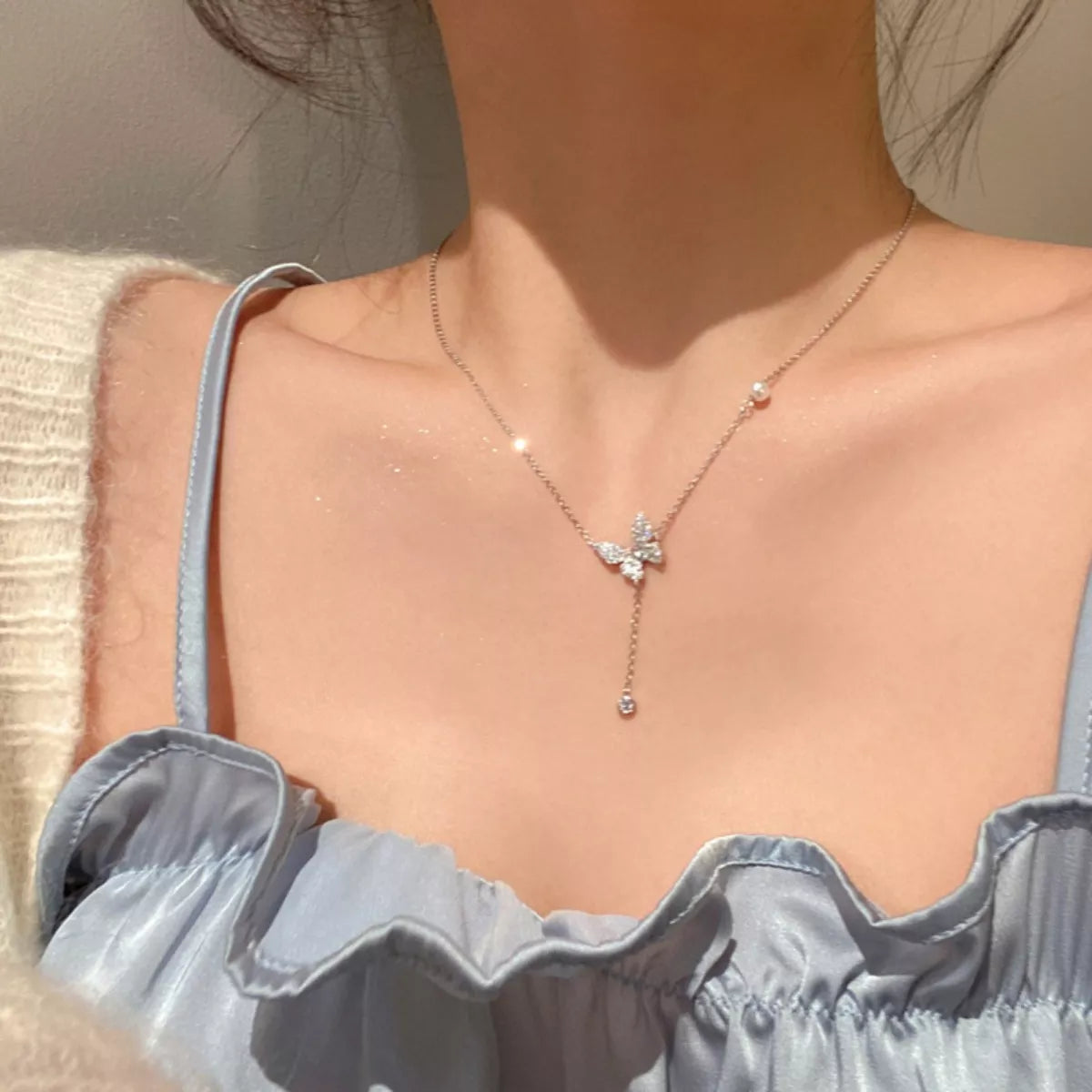 Necklace with a butterfly pendant worn by a person in a light blue top.