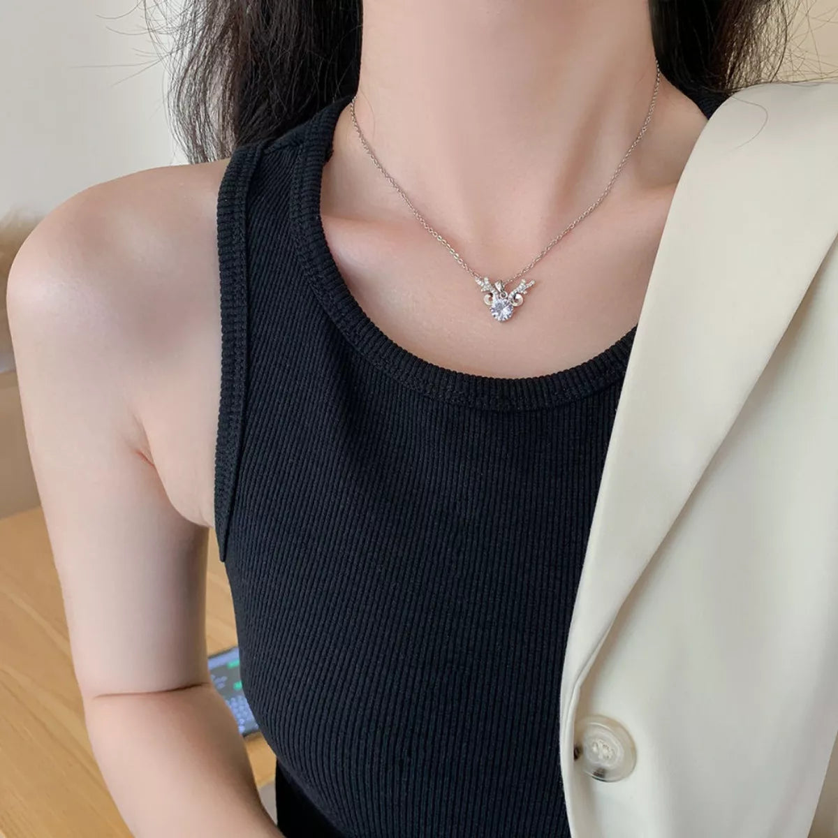 Person wearing a black top and beige blazer with a necklace featuring a heart pendant.