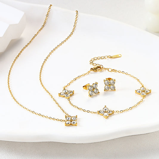 Gold French baby's breath flower necklace, bracelet, and earrings set with clear zircon stones on a white display surface.