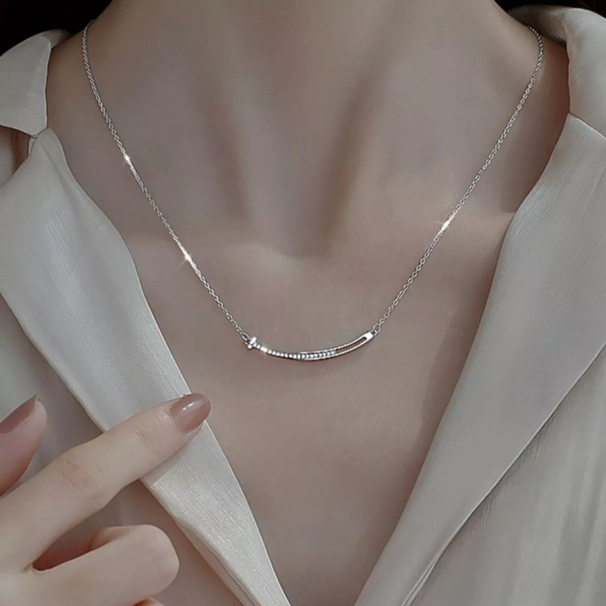 Silver necklace being worn on a person with a neutral background