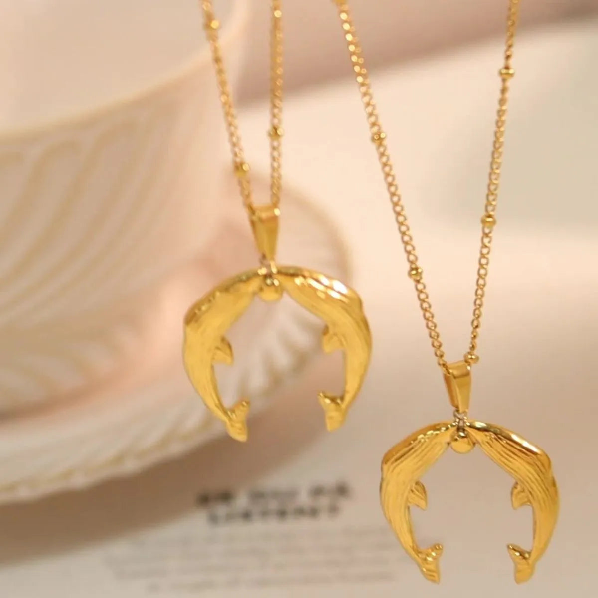 Two gold necklaces with unique pendants on a soft beige background