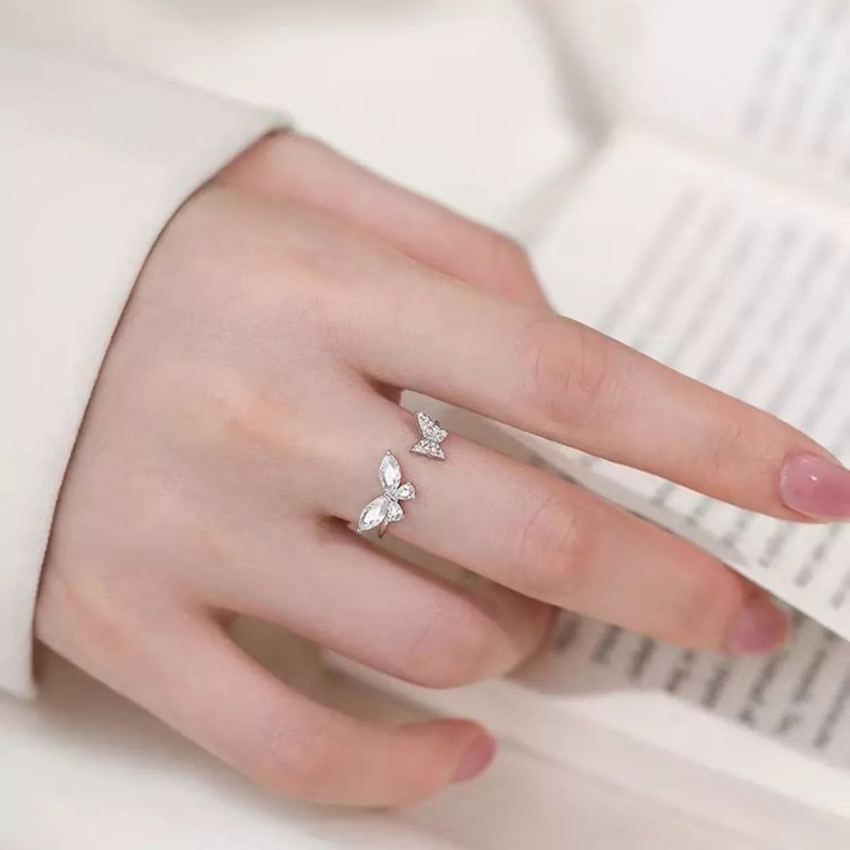 Hand wearing a silver ring with a butterfly design on a light background