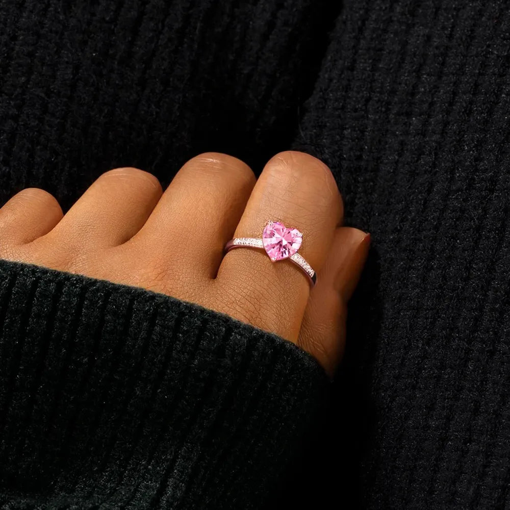 Heart-shaped pink gemstone ring on a person's finger against a black background