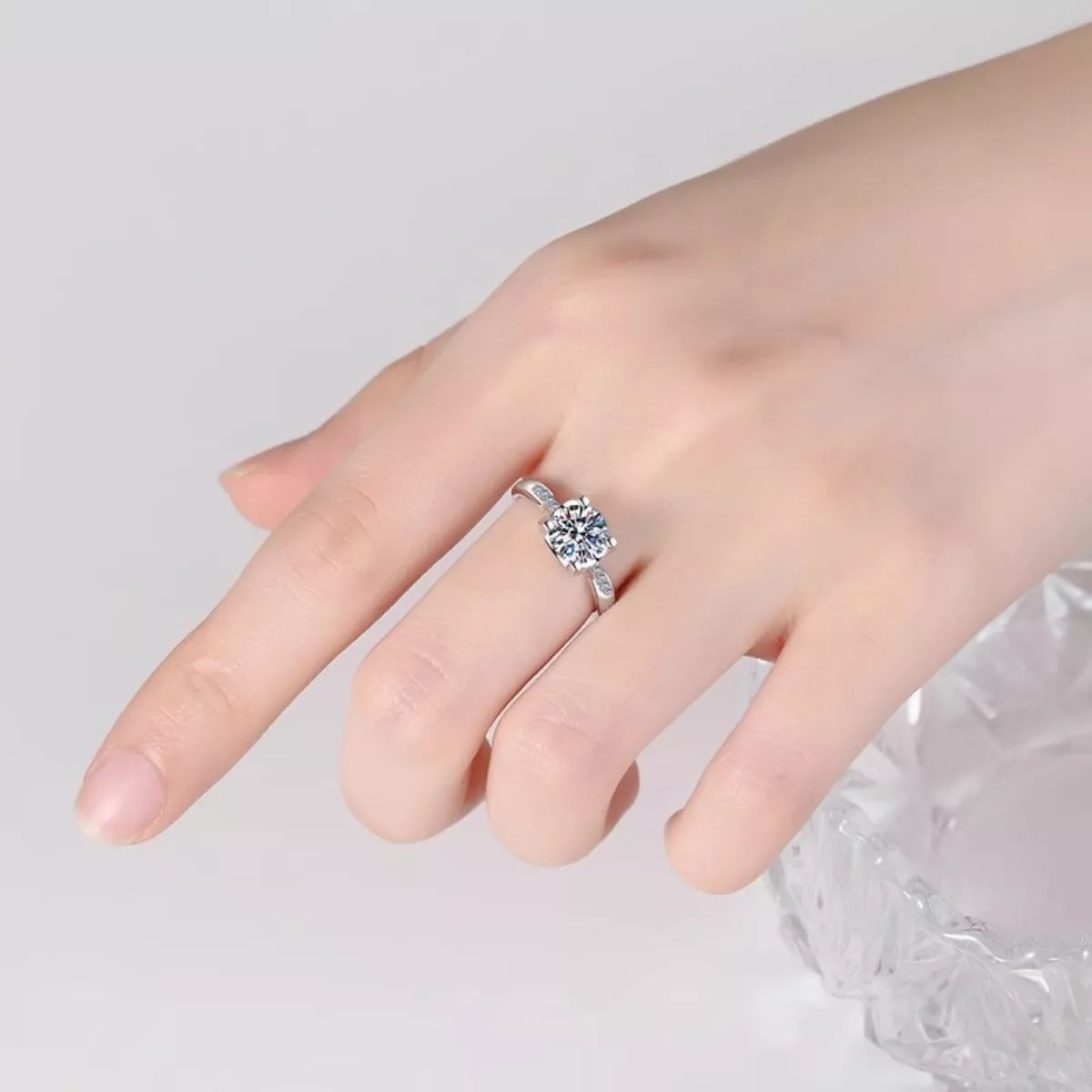 Silver ring with a heart-shaped gemstone on a hand against a light gray background