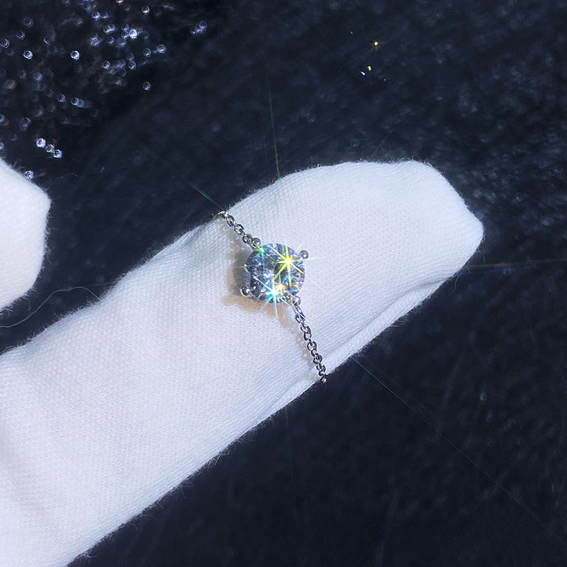 A silver ring with a round clear gemstone displayed on a white gloved finger against a dark textured background.