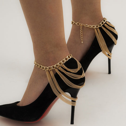 Black high-heeled shoes with gold chain accessories on a neutral background