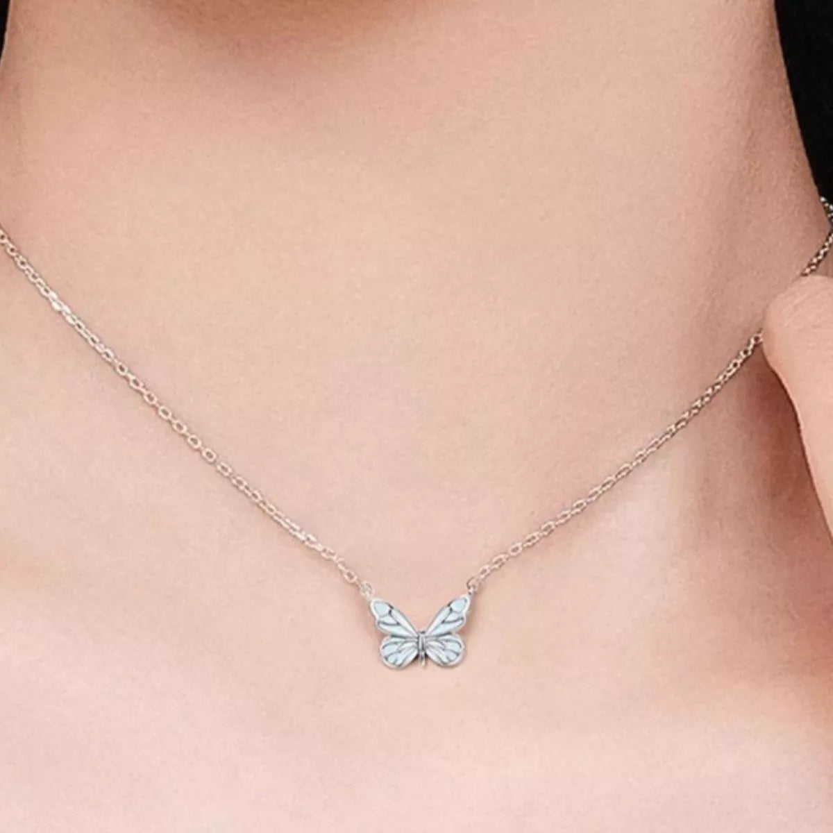 Silver butterfly necklace on a person's neck against a neutral background