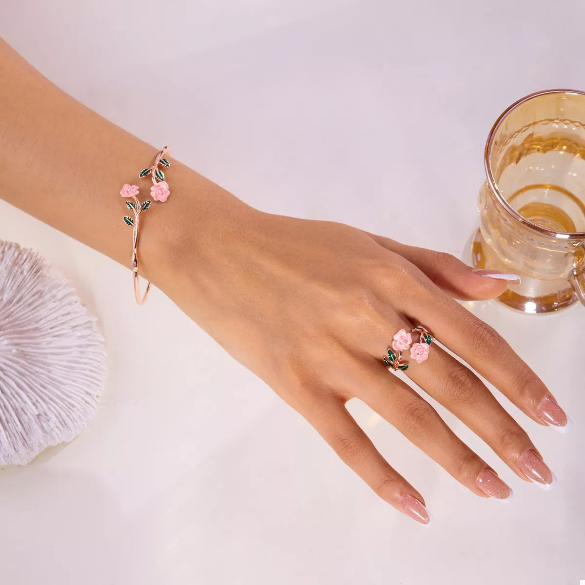 Hand wearing a floral bracelet and ring with a glass of water on a light background