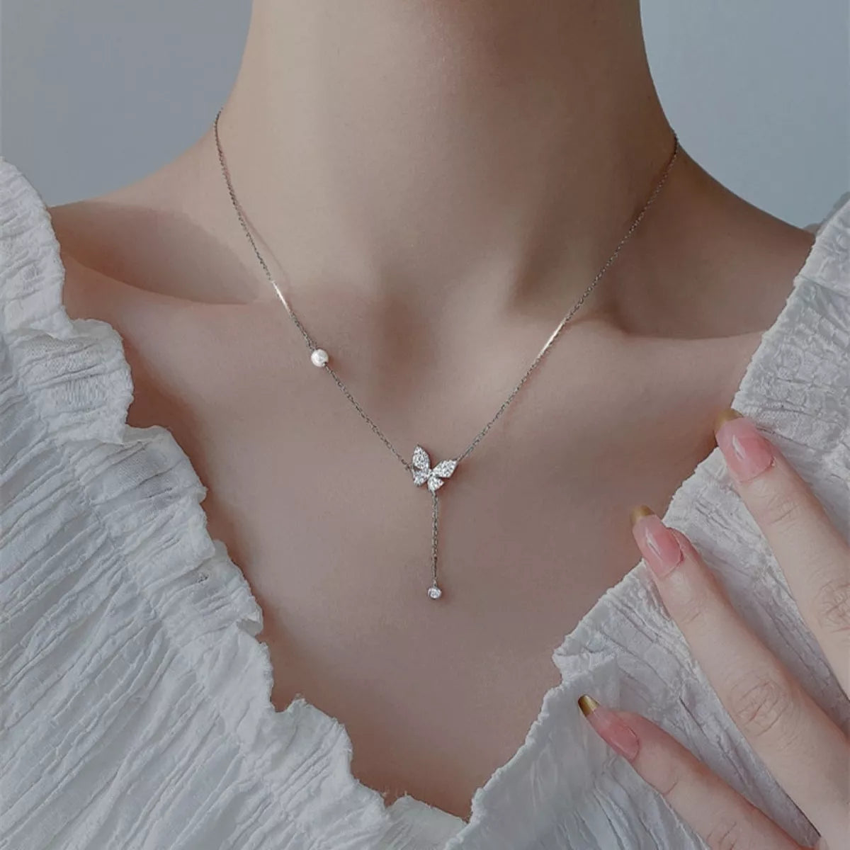 Butterfly necklace with pearls on a person wearing a light-colored top.