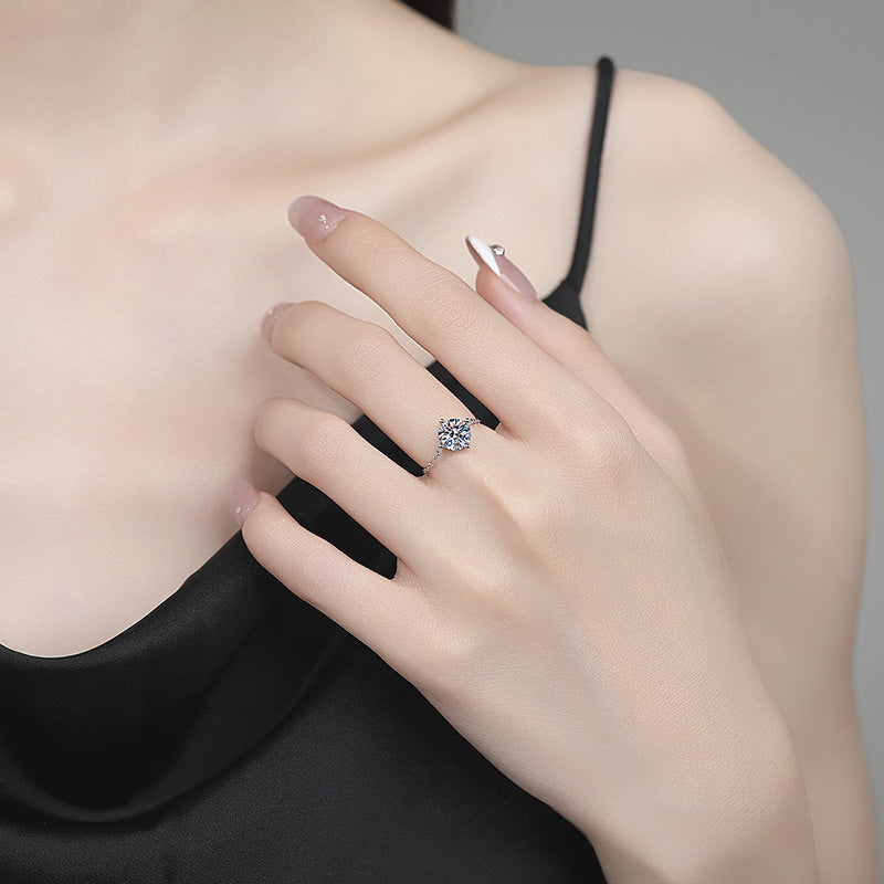 A close-up lifestyle shot of a model's hand wearing a silver-toned halo ring with clear gemstones, styled with a black spaghetti-strap top against a neutral gray background.
