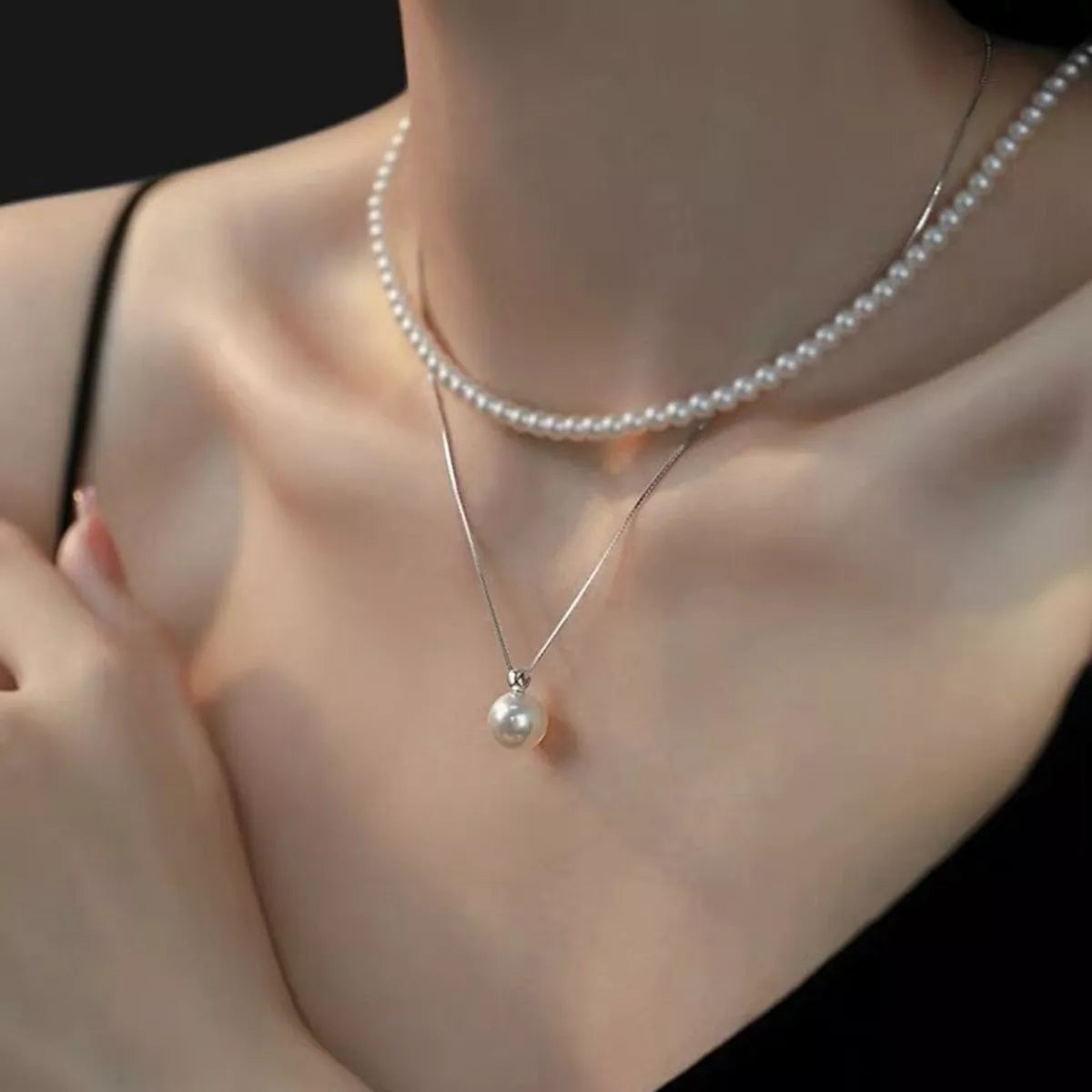 Pearl necklace with a pendant on a person wearing a black top.