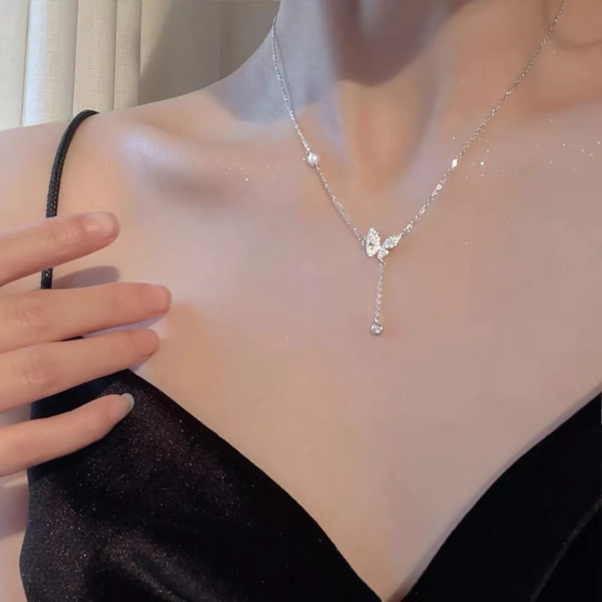 Silver butterfly necklace on a mannequin with a hand adjusting it.