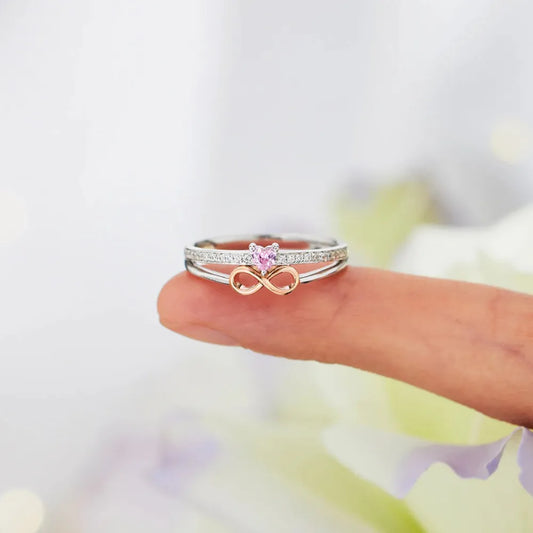 Two rings, one with a heart and the other with an infinity symbol, on a blurred background.