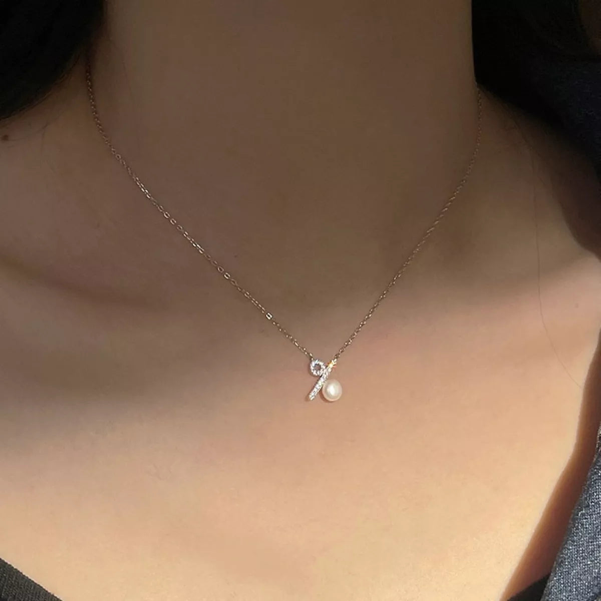 Necklace with a pendant featuring a pearl and small heart on a person's neck.