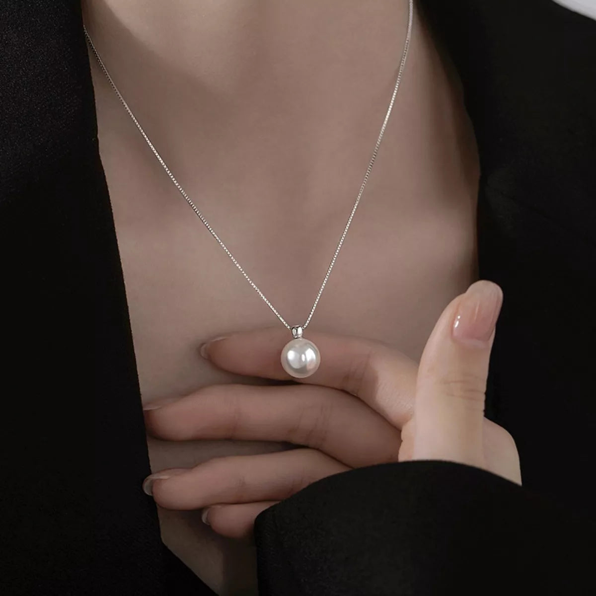 Pearl necklace with a hand holding it against a neutral background