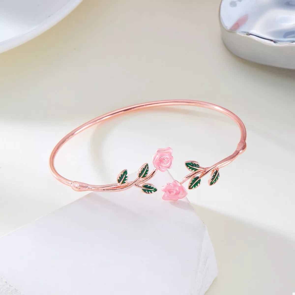 Rose gold bracelet with pink roses and green leaves on a white surface