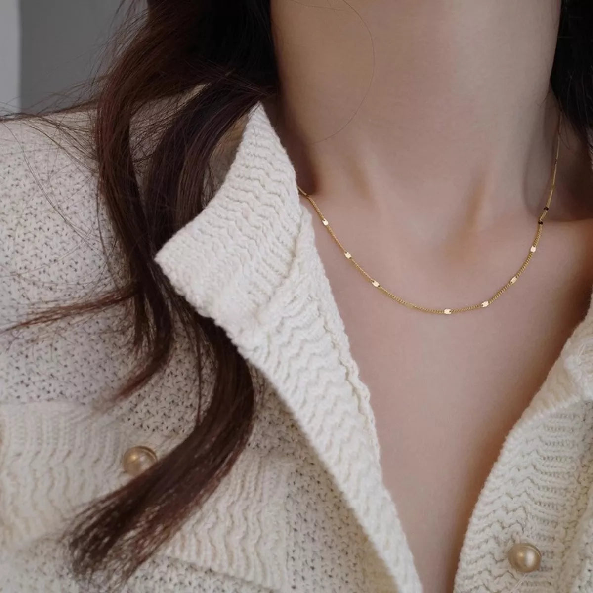 Close-up of a person wearing a delicate gold necklace with a neutral background