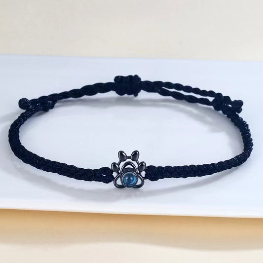 Black braided bracelet with a silver and blue charm on a light background