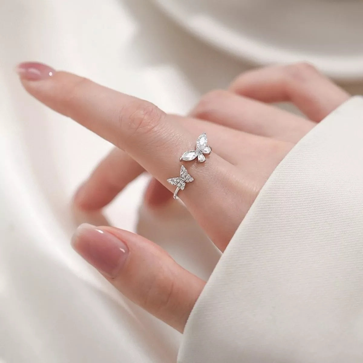 Butterfly-shaped silver ring on a finger against a neutral background