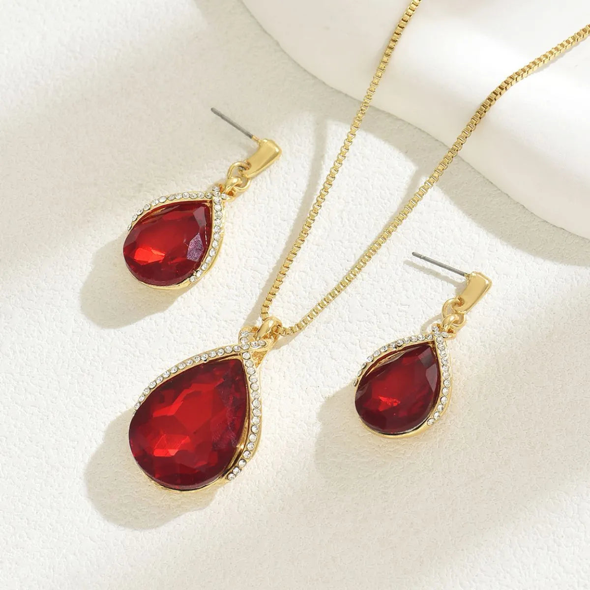Jewelry set with red teardrop-shaped stones and gold chains on a white background