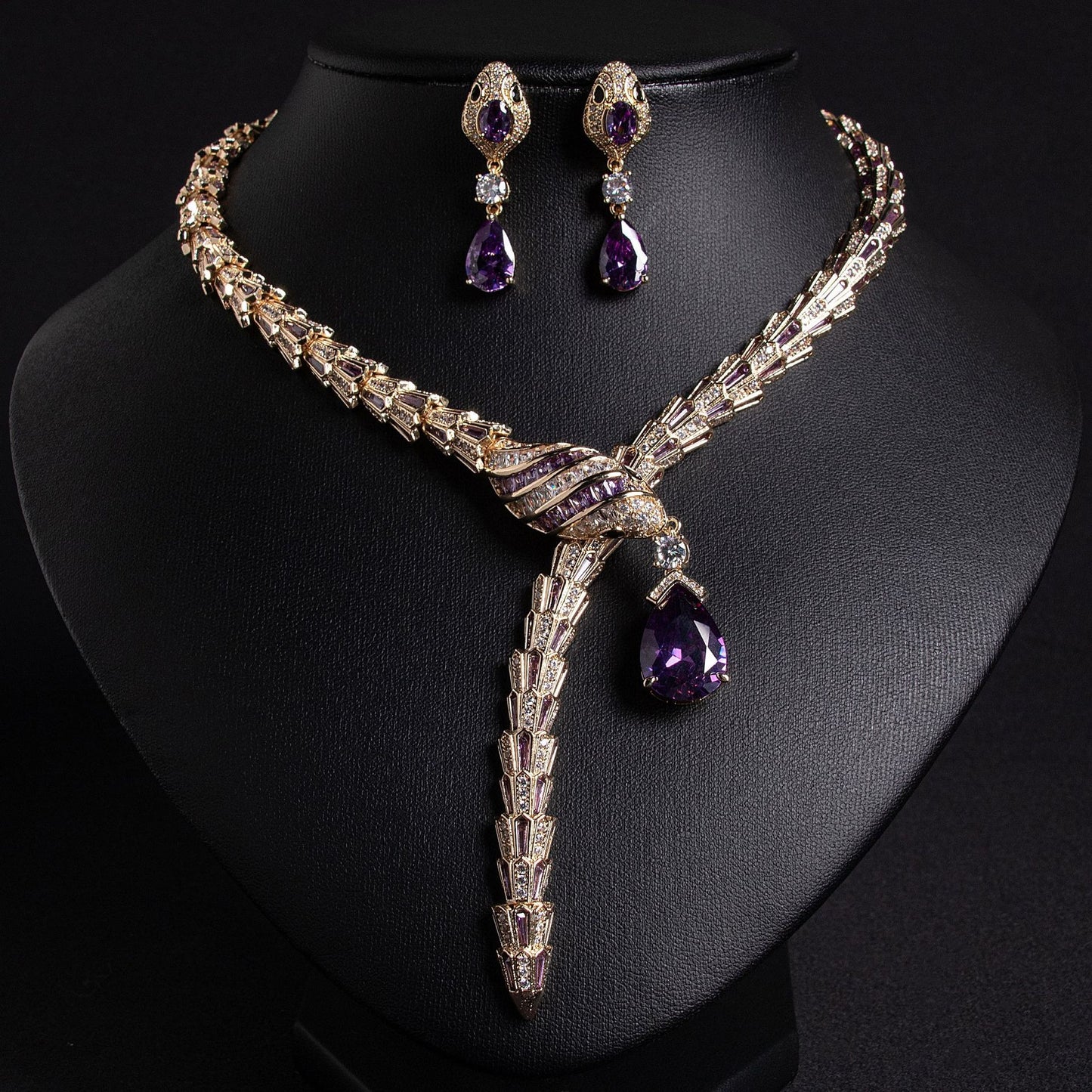 Gold snake necklace and earrings set with purple and clear stones, on a black bust.