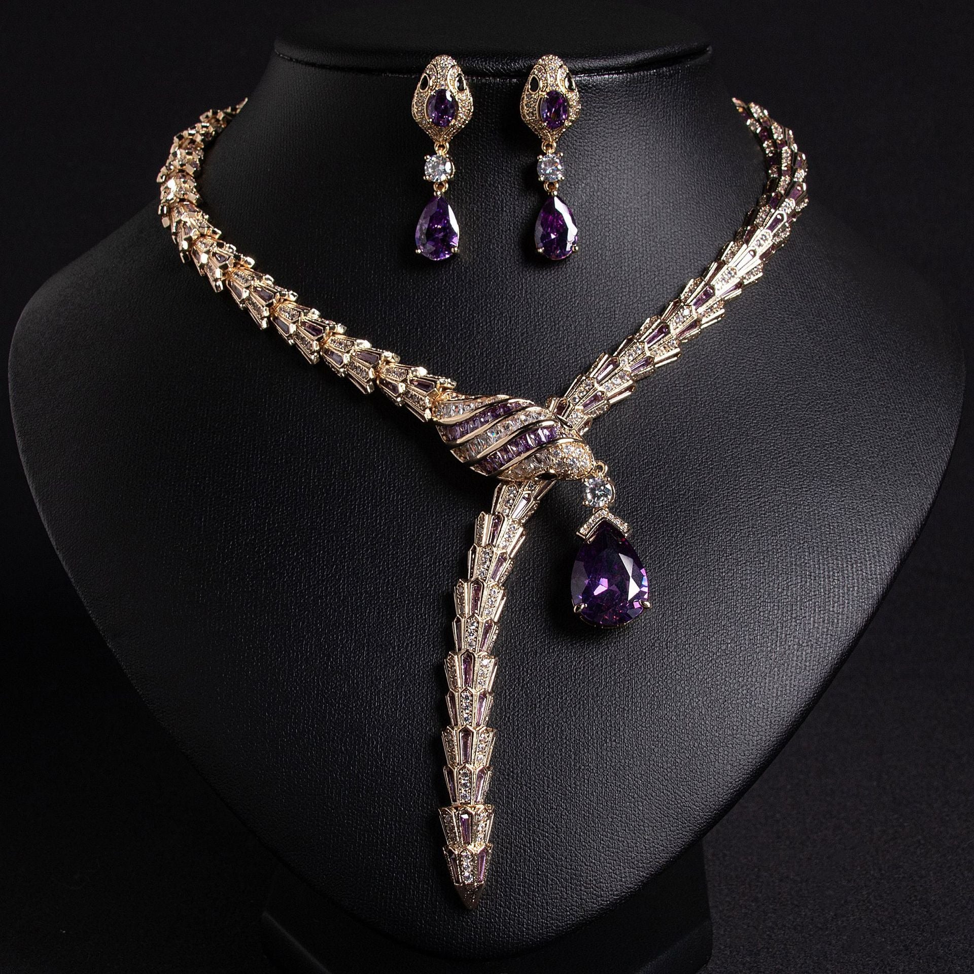 Gold snake necklace and earrings set with purple and clear stones, on a black bust.