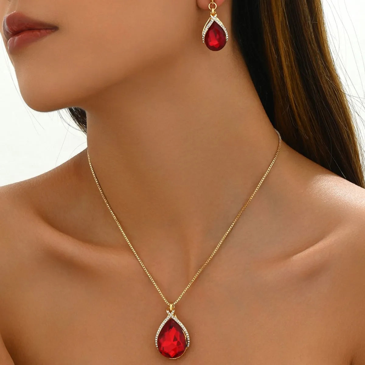 Gold necklace and earrings with red gemstones on a model against a neutral background